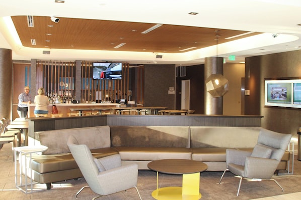 Un vestíbulo moderno con zona de bar, asientos y una pantalla de televisión.