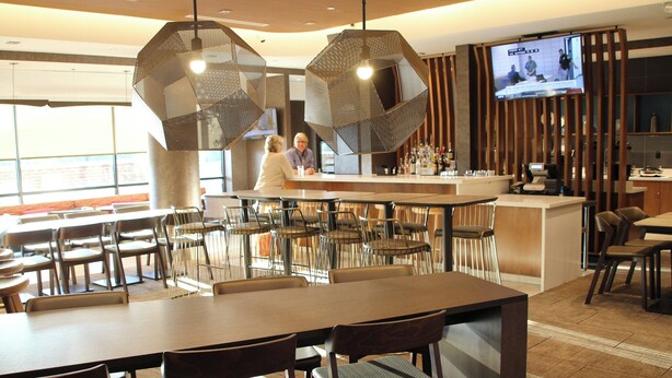Un restaurante moderno con mesas y sillas altas, una zona de bar y una pantalla de televisión que muestra un noticiero.