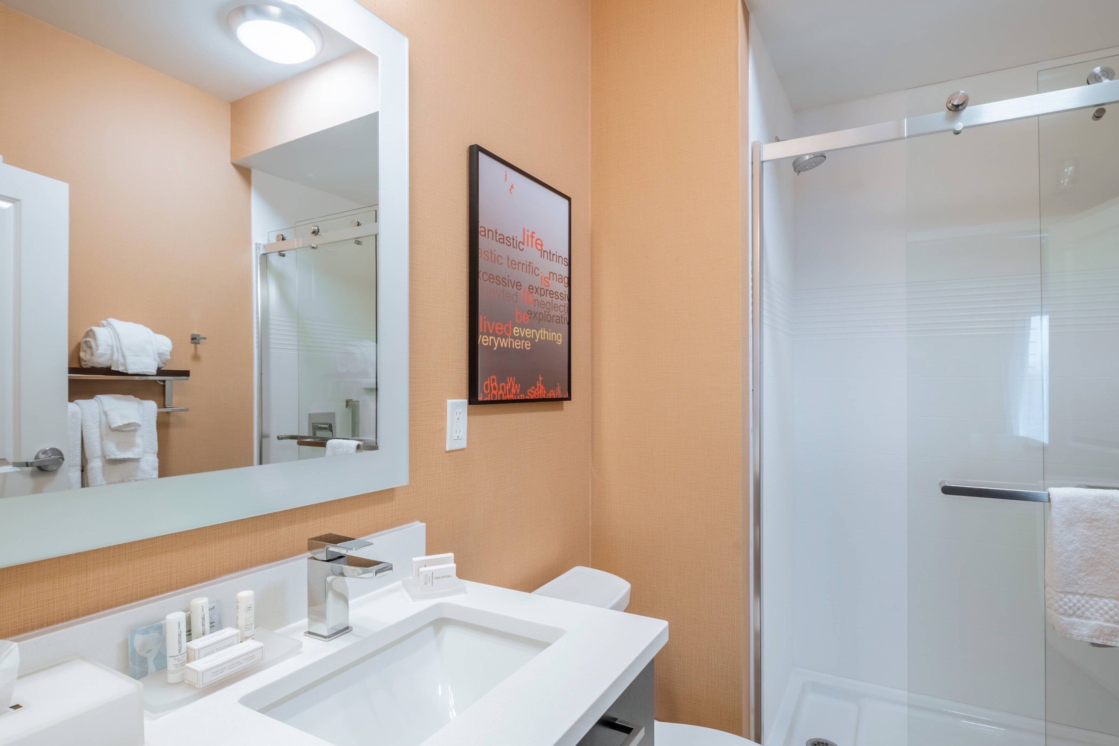 A bathroom with a large mirror, a sink, a toilet, and a glass shower enclosure.