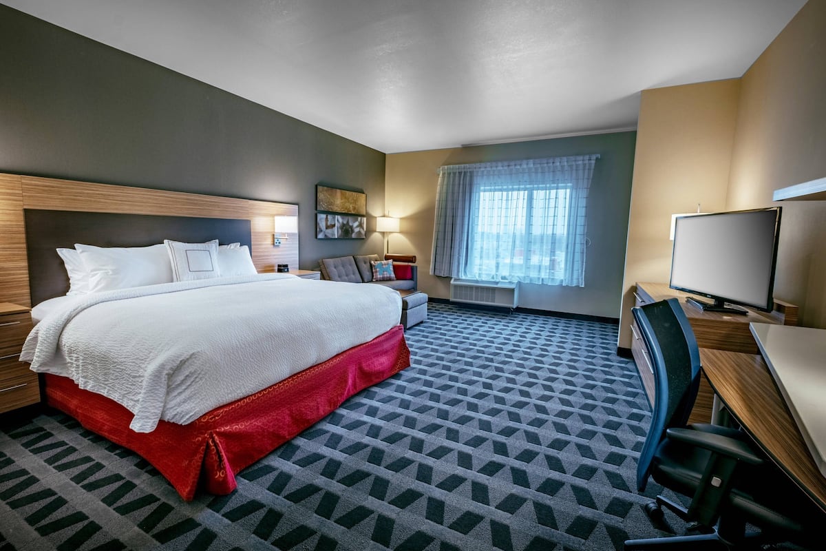 A hotel room with a large bed, a desk, a chair, a television, and a window with curtains.