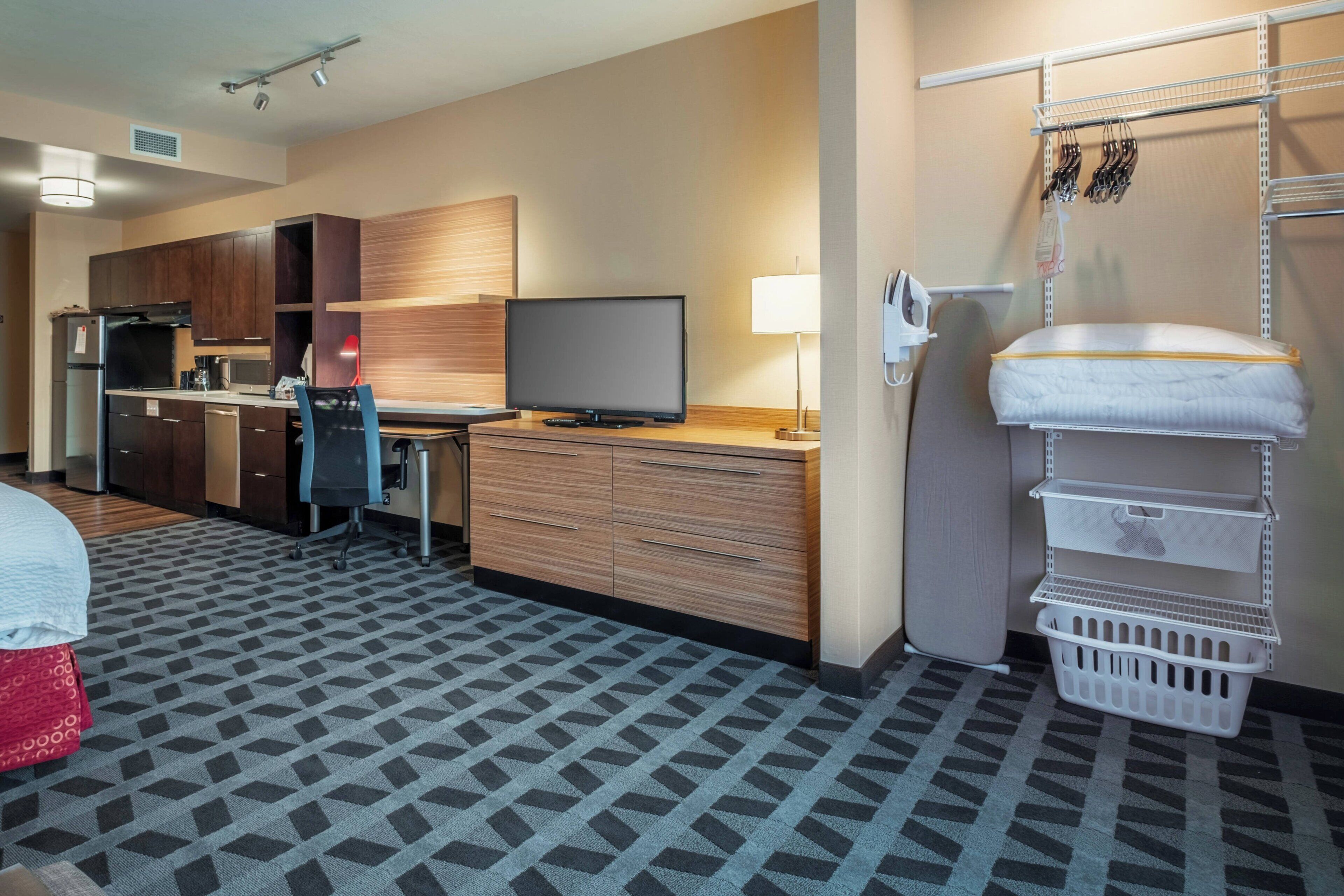 A hotel room with a kitchenette, a TV, a desk, and a bed.