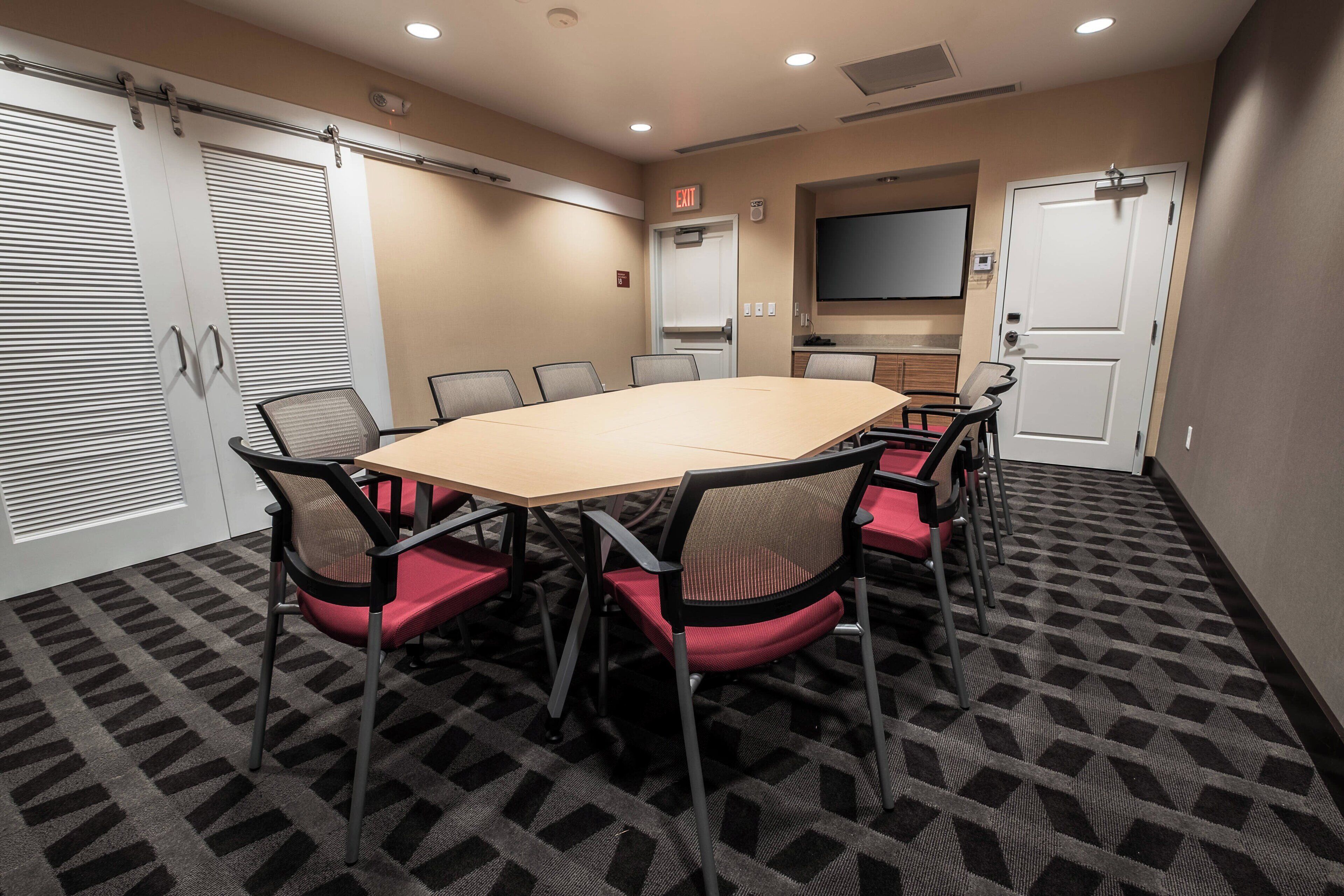 A conference room with a large table, chairs, a TV, and an exit sign.