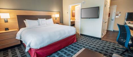 A hotel room with a large bed, a desk, a TV, and a bathroom visible through an open door.