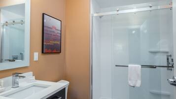 Un baño moderno con un espejo grande, dos lavamanos, una cabina de ducha con mampara de vidrio y un cartel motivacional en la pared.