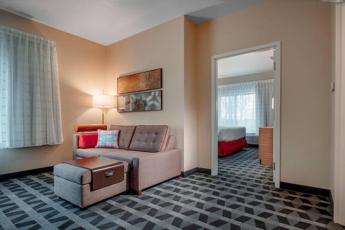 A hotel room with a sofa, a small table, a lamp, and a mirror.