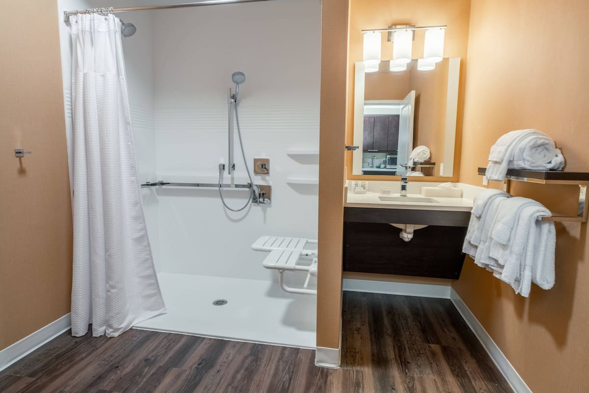 A bathroom with a shower, a sink, a mirror, and a towel rack.