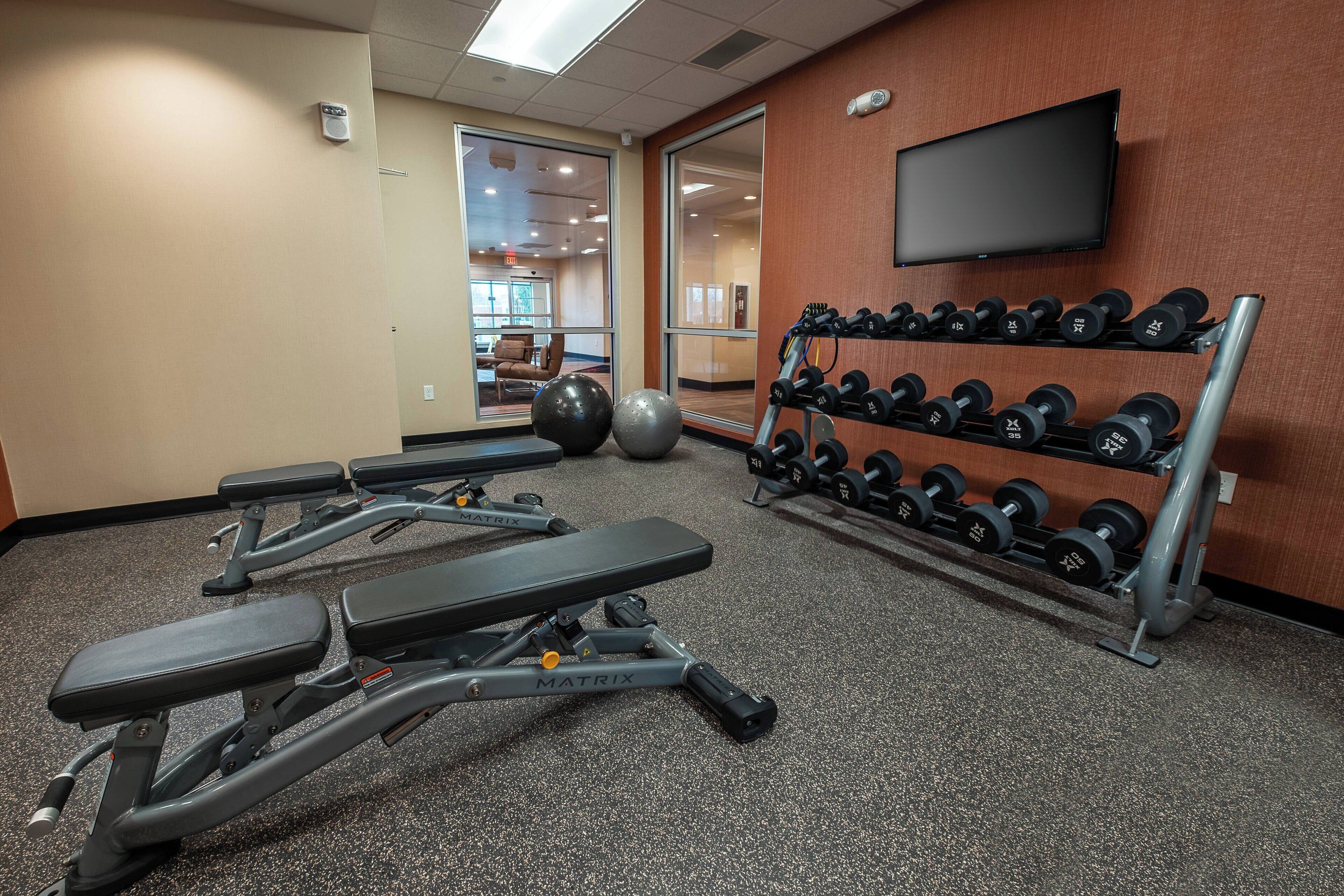A gym with weight benches, dumbbells, and exercise balls.