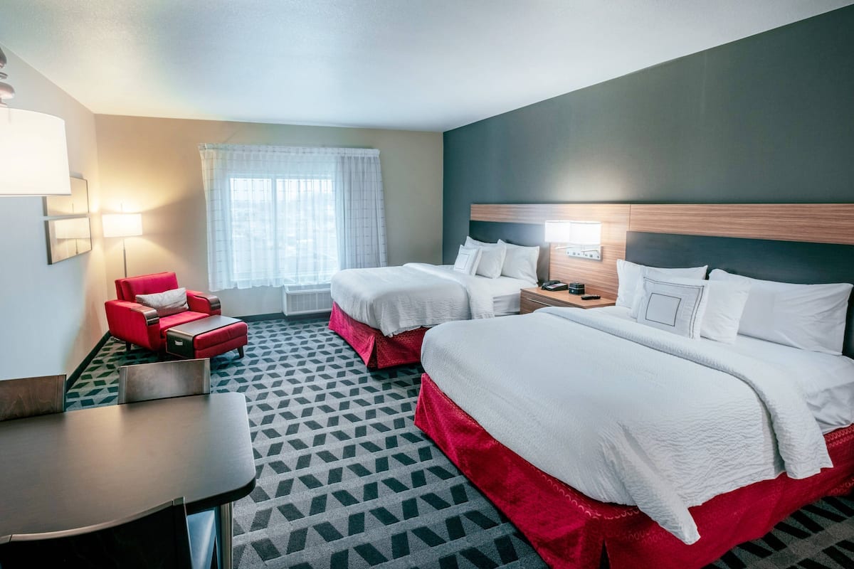 A hotel room with two beds, a red armchair, a small table, and a window with curtains.