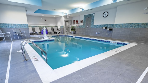 An indoor swimming pool with a tiled floor, a metal pool ladder, and lounge chairs. - TownePlace Suites Toledo Oregon (Oregon)