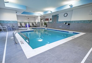 An indoor swimming pool with a tiled floor, a metal pool ladder, and lounge chairs. - TownePlace Suites Toledo Oregon (Oregon)