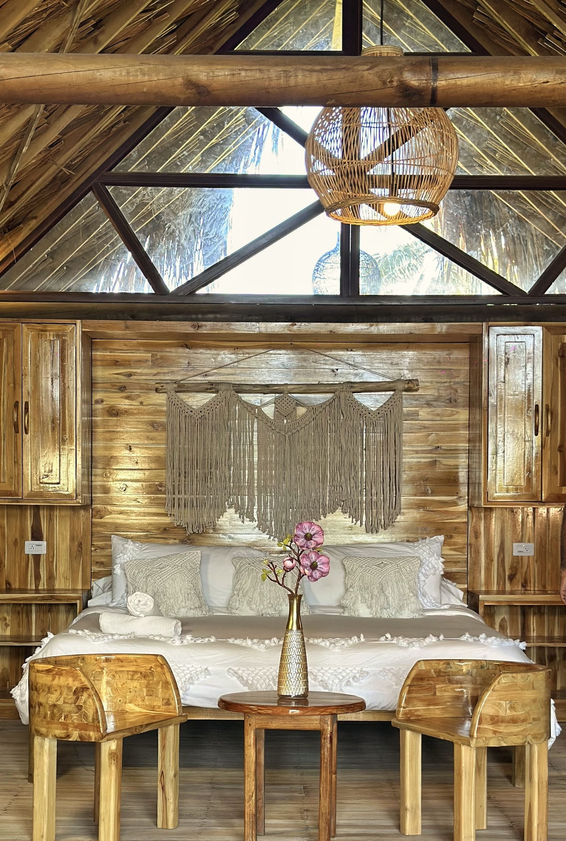 Une pièce chaleureuse aux murs en bois, avec un lit, une décoration murale en macramé et un luminaire suspendu.