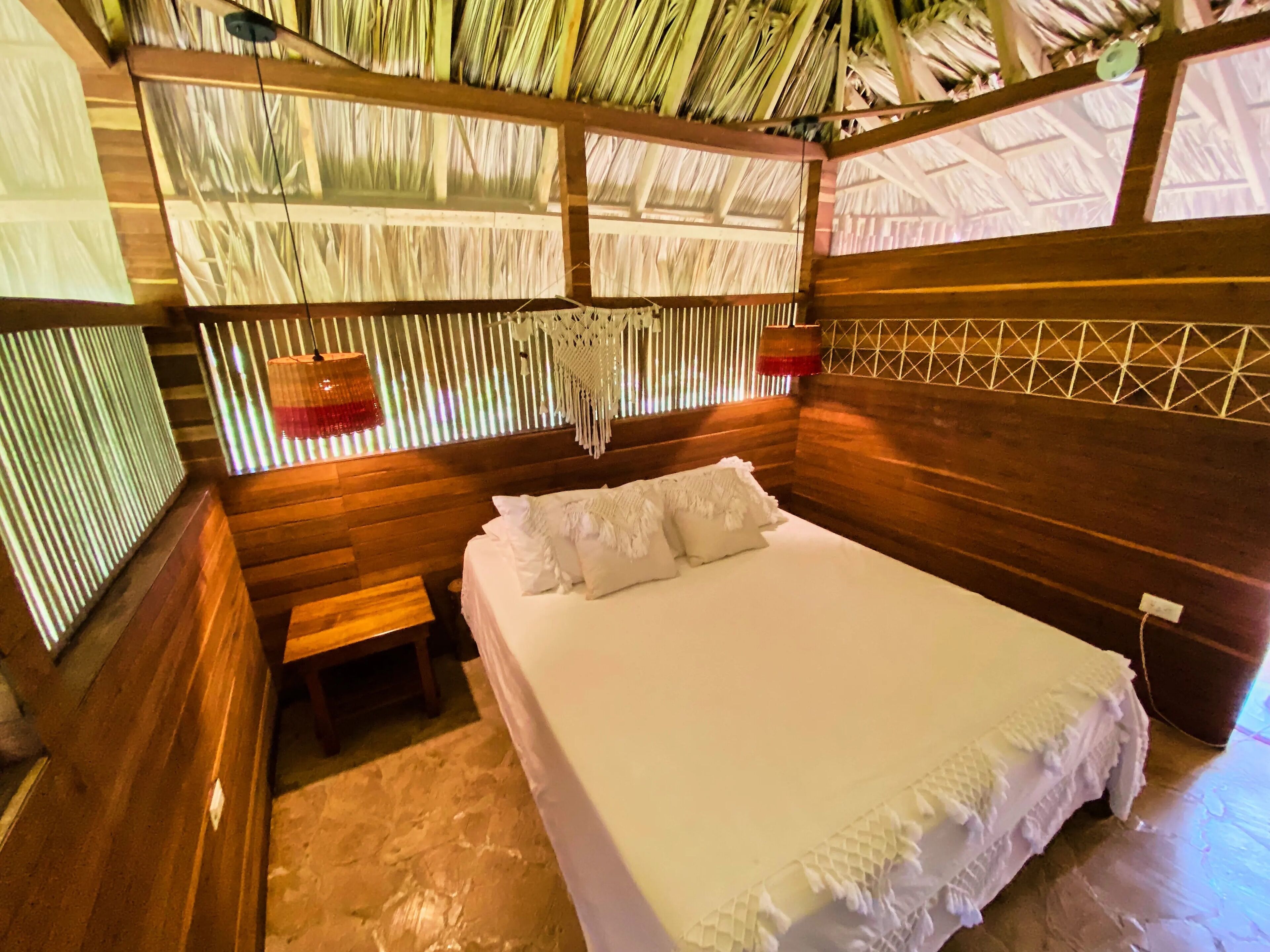 A room with a bed, wooden walls, a bench, and a thatched roof.