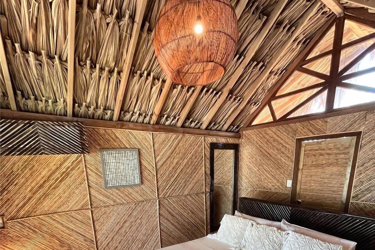 A room with a bed, a woven ceiling, a hanging light fixture, and a mirror on the wall.