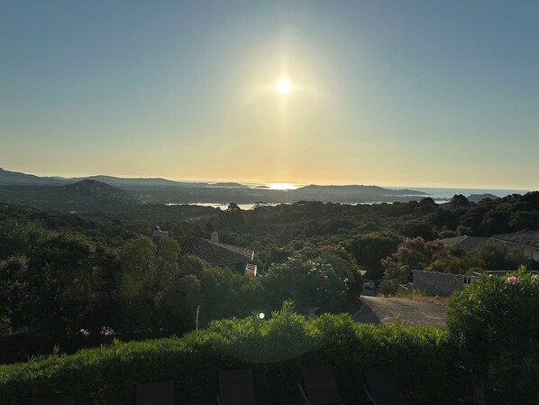 A panoramic view of a residential area with houses, trees, and a distant body of water under a clear sky.
