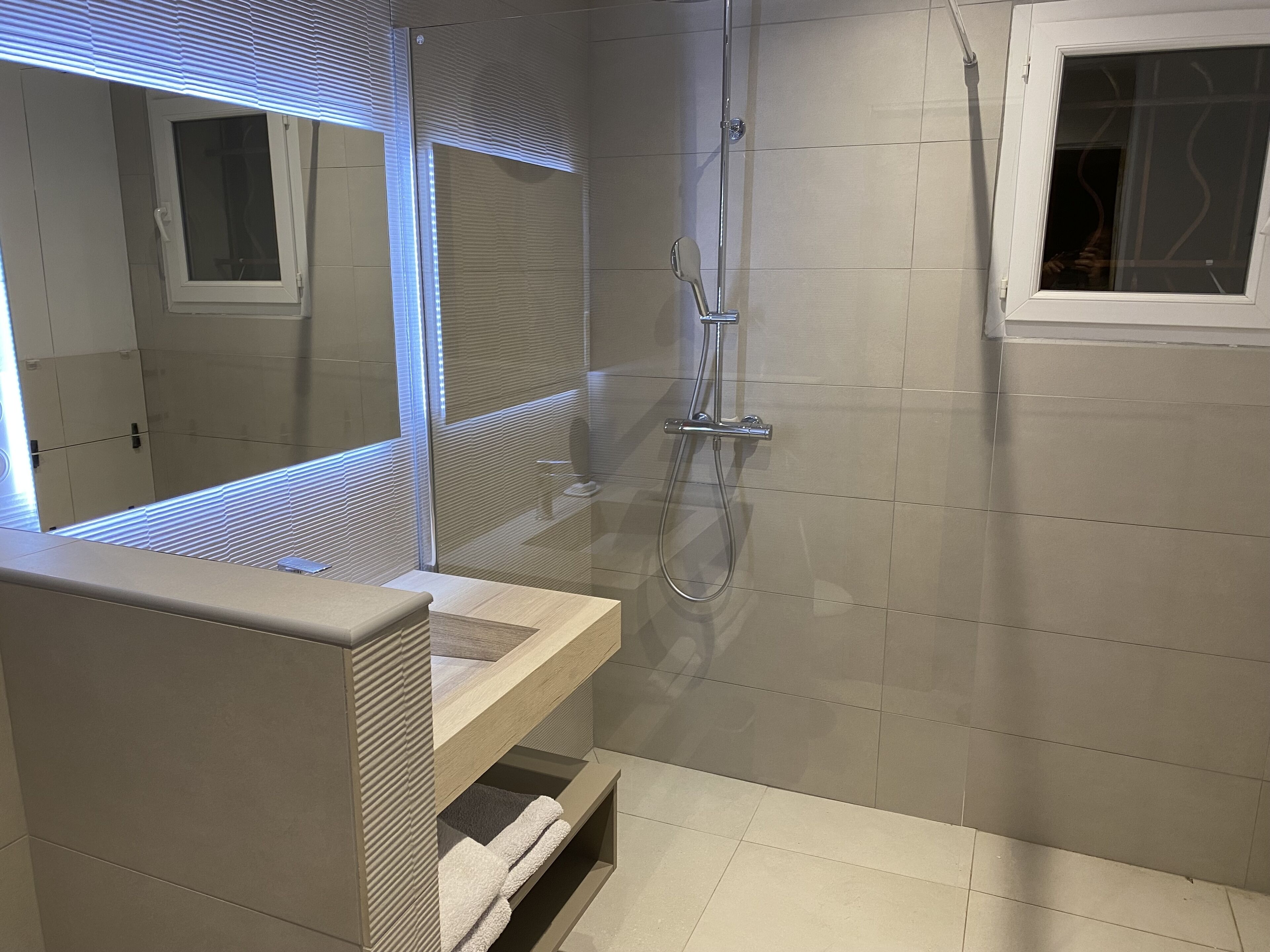 Ein modernes Badezimmer mit Duschkabine aus Glas, einem Waschtisch mit Spiegel und einem Fenster mit Jalousien.