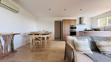 A modern, open-plan living space with a dining area, kitchenette, and a large bed with multiple pillows.