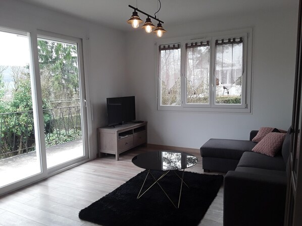 A modern living room with a flat-screen TV on a wooden cabinet, a black round coffee table, a dark grey sofa, and a black rug.