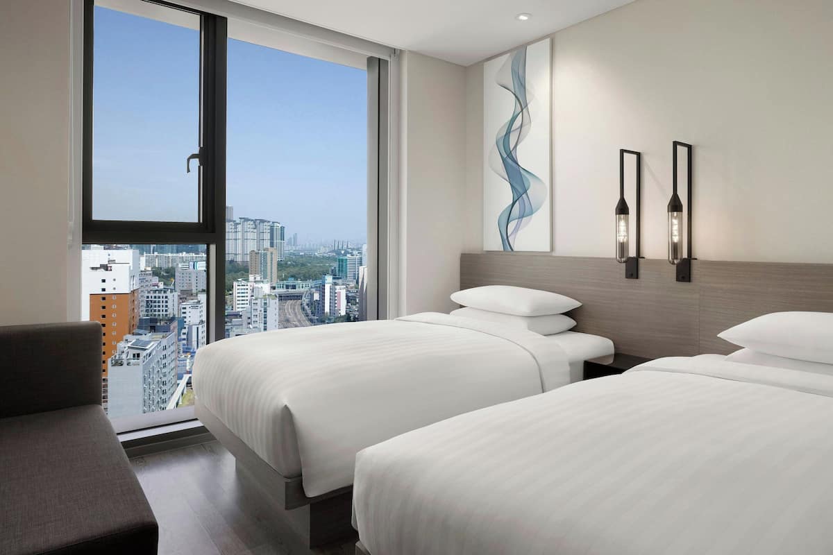 A hotel room with two beds, a view of the city through large windows, and modern wall art.