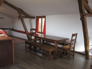 A rustic dining room with a wooden table and benches, a ladder, and a window with red curtains.