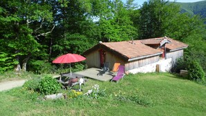 A rustic cabin with a tiled roof, surrounded by lush greenery and a red umbrella. - Gites des Pics: the Black Pic - panoramic view (Riverenert)