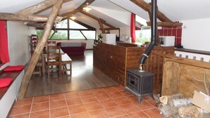 A rustic kitchen with a wood-burning stove, wooden beams, and a dining area with a red sofa. - Gites des Pics: the Black Pic - panoramic view (Riverenert)