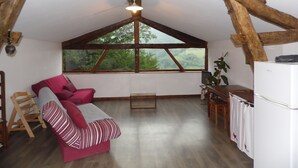 A cozy loft-style room with a wooden ceiling, a sofa, a dining table, and a refrigerator. - Gites des Pics: the Black Pic - panoramic view (Riverenert)