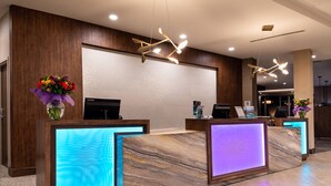 Un espace d’accueil doté de comptoirs en marbre, d’un lustre moderne et d’un grand écran fixé au mur.