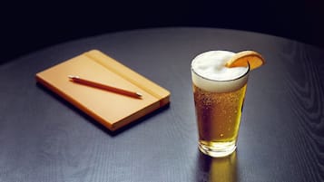 A glass of beer with a slice of orange on a dark wooden table.