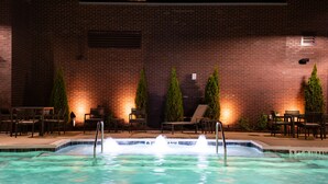 Une piscine avec un mur en briques et des chaises longues à l’arrière-plan.