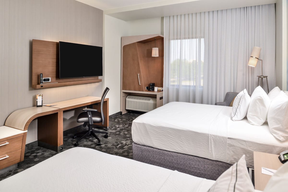 Une chambre d’hôtel équipée d’un téléviseur à écran plat, d’un bureau avec une chaise, de deux lits, d’une armoire et d’une table de chevet avec une lampe.