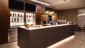 Un espace bar moderne doté d’un long comptoir, d’une cave à vin et d’une machine à café.