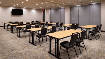 A conference room with multiple tables and chairs, a flat-screen TV mounted on the wall, and a patterned carpet.