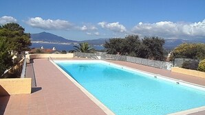 Ein rechteckiger Schwimmteich mit klarem, blauem Wasser, umgeben von einer gefliesten Liegefläche und einem Metallgeländer.
