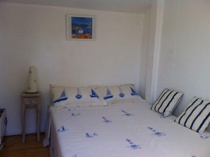 A bedroom with a bed featuring a nautical theme, a small bedside table with a lamp, and a framed picture on the wall.