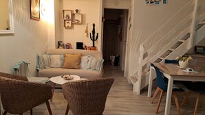 Ein gemütliches Wohnzimmer mit einer Couch, Korbstühlen, einem kleinen runden Tisch und einer Treppe, die eine weitere Ebene hinaufführt.