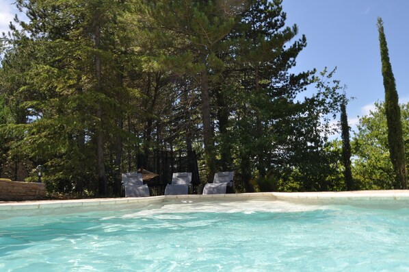 A swimming pool with lounge chairs and a stone wall, surrounded by tall trees.