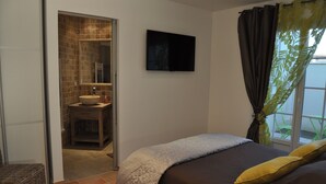 A bedroom with a bed, a TV mounted on the wall, a bathroom with a sink and mirror, and a window with curtains.