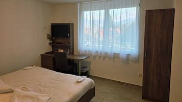 Una habitación de hotel con cama, escritorio, silla, televisor y armario.