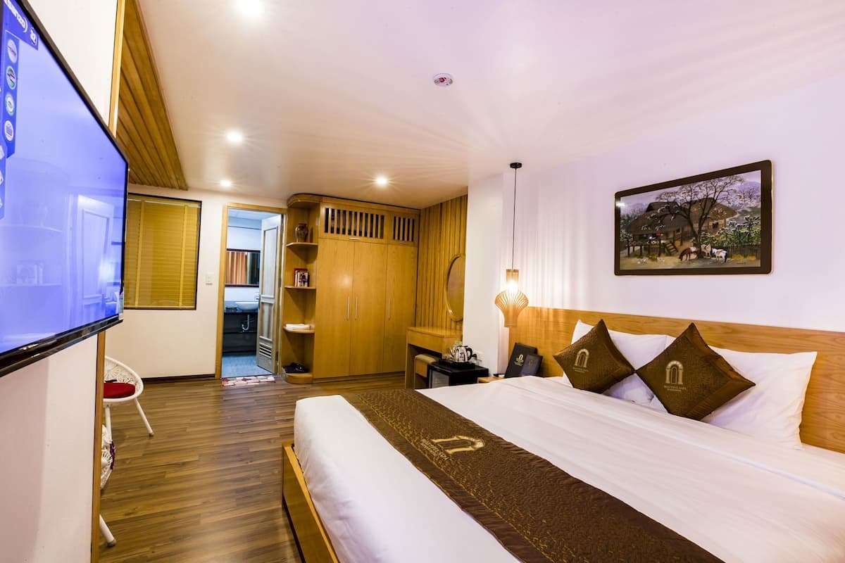 A hotel room with a bed, a TV, a desk, a chair, a wardrobe, and a painting on the wall.