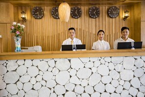 A reception desk with three staff members, wooden paneling, stone wall, and multiple clocks on the wall. - BEAUTIFUL SAPA HOTEL (Sa Pa)