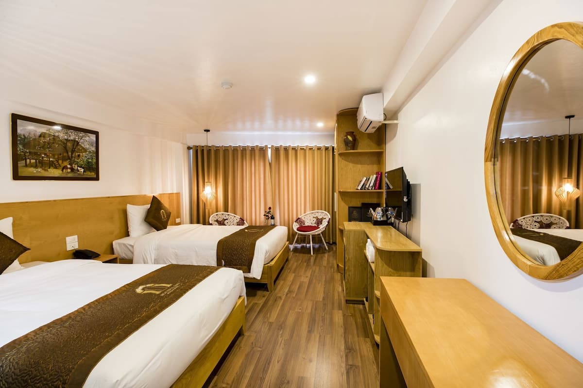 A hotel room with two beds, a wooden headboard, a desk, a chair, a TV, a mirror, and a painting on the wall.