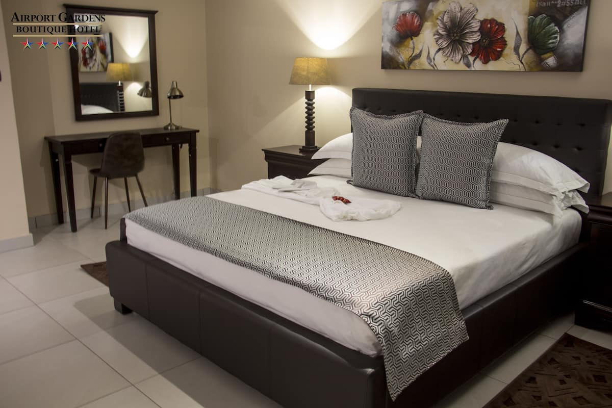 A hotel room with a large bed, a desk, a chair, a lamp, and a painting on the wall.