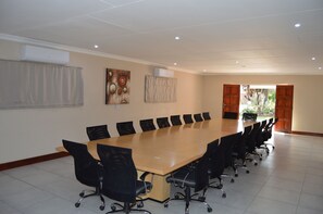 Uma sala de conferência com uma mesa comprida, cadeiras pretas e dois aparelhos de ar condicionado na parede.