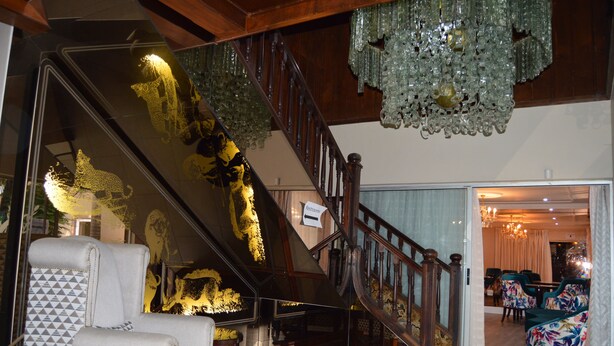 A grand staircase with a chandelier, a patterned armchair, and a view into a dining area.