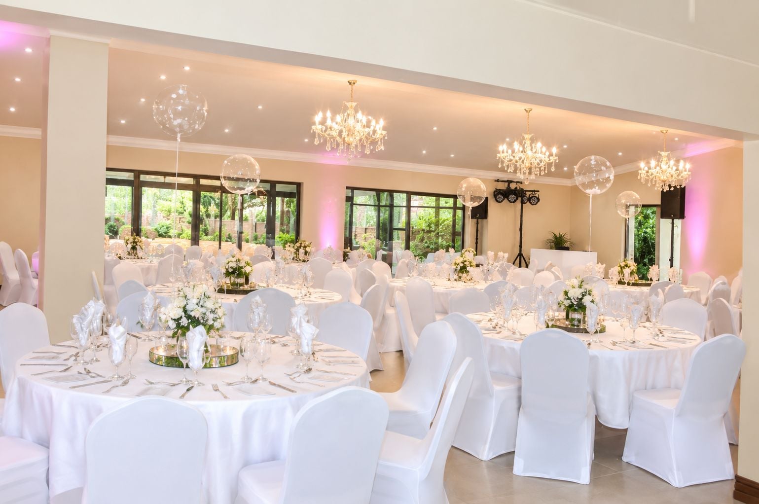 A banquet hall with round tables, white chairs, and chandeliers.