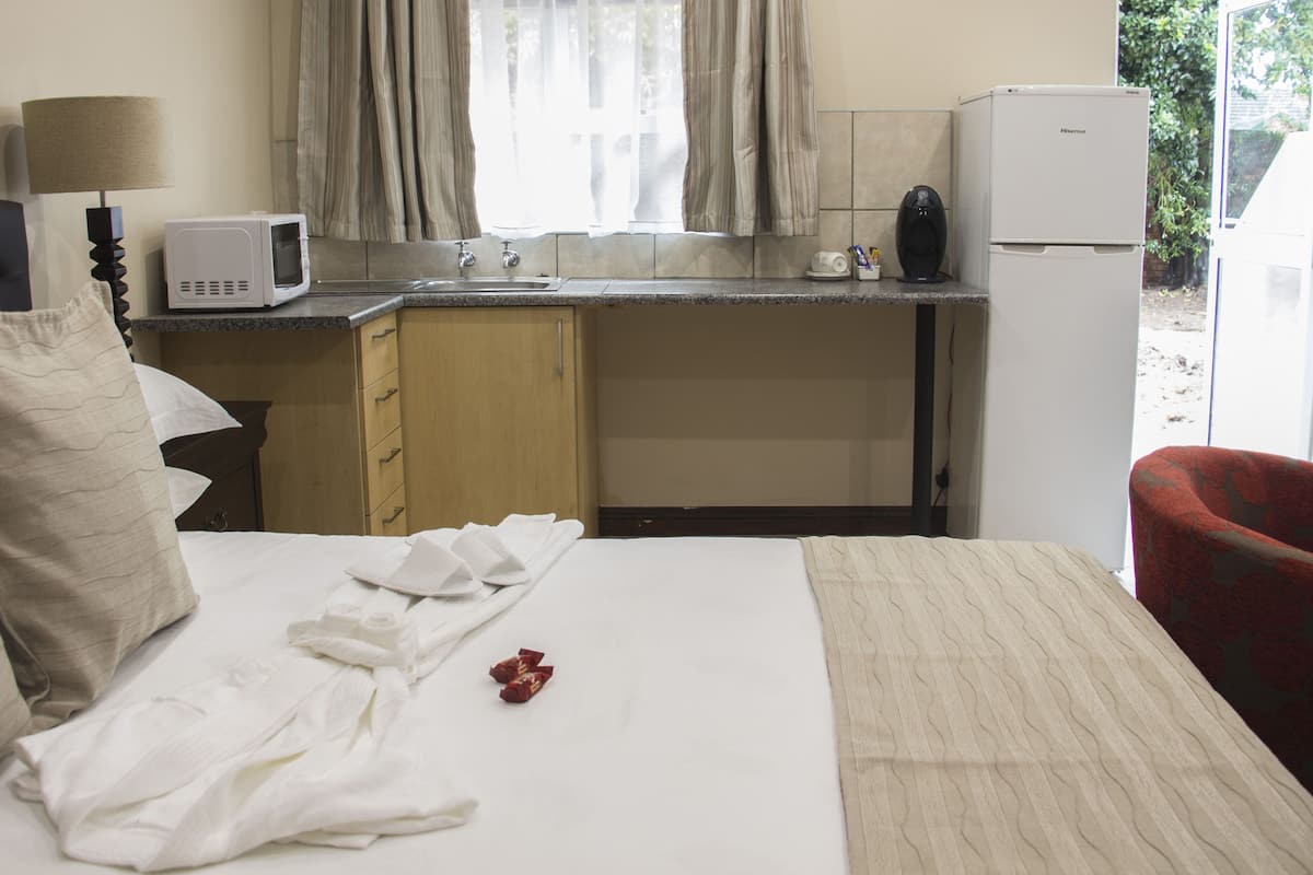 A hotel room with a bed, a desk with a microwave, a refrigerator, and a window with curtains.