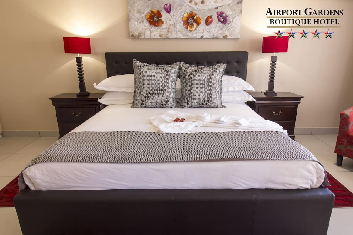 A neatly made bed with patterned pillows and a red throw blanket, flanked by two bedside tables with lamps, in a hotel room.