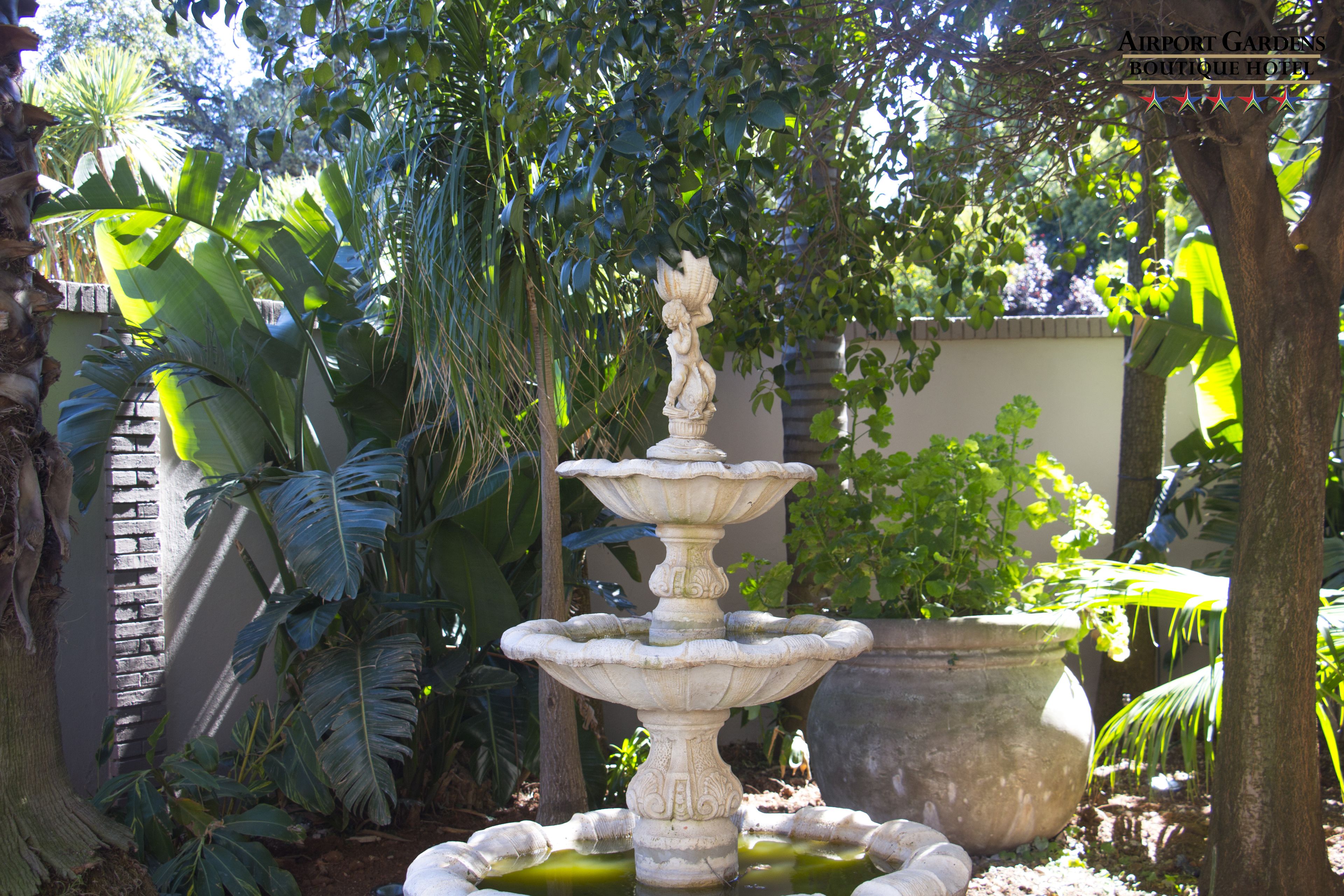 Uma fonte de pedra em vários níveis, rodeada por exuberante vegetação tropical num jardim.