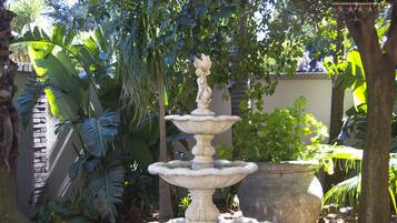 Uma fonte de pedra em vários níveis, rodeada por exuberante vegetação tropical num jardim.