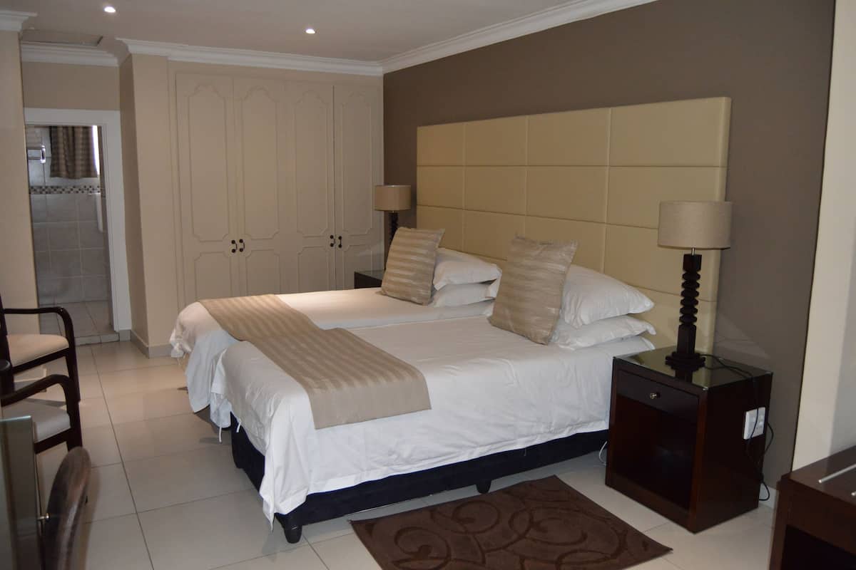 A double bed with a beige headboard, two bedside tables with lamps, a wooden chair, and a wardrobe.